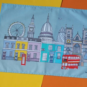 May include: A blue tea towel with a colorful illustration of London landmarks, including Big Ben, the London Eye, St. Paul's Cathedral, and a red double-decker bus. The text "Helena Carrington" is printed in the bottom right corner.