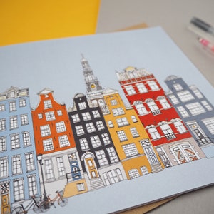May include: A colorful illustration of a row of buildings with a blue sky background. The buildings are drawn in a cartoon style and have different colors, including red, yellow, blue, and black. There are bicycles in front of the buildings.
