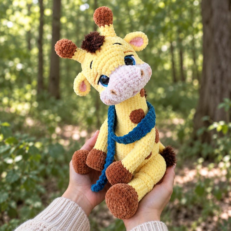 May include: A crocheted giraffe plush toy with yellow yarn, brown spots, and a brown tuft on its head. The giraffe has a light pink muzzle, large blue eyes, and brown feet. It wears a long, textured blue scarf wrapped around its neck.