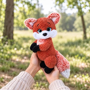 May include: A plush crochet fox toy featuring a vibrant orange body, a white chest and muzzle, and black paws. The stuffed animal has large, expressive blue eyes, a small black nose, and a bushy tail with a white tip, crafted from soft yarn.
