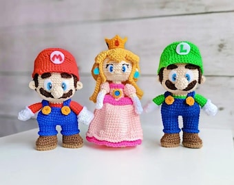Pode incluir: Três brinquedos de pelúcia de crochê: Mario, Peach e Luigi. Mario está usando um chapéu vermelho e um macacão azul. Peach está usando um vestido rosa e uma coroa. Luigi está usando um chapéu verde e um macacão azul.