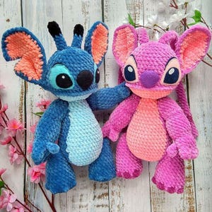 Puede incluir: Dos juguetes de peluche tejidos a crochet, uno azul y otro rosa, que se asemejan a los personajes Stitch y Angel de la película de Disney Lilo & Stitch. Los juguetes tienen ojos grandes, bocas cosidas y pelaje texturizado.