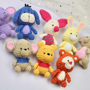 Op de afbeelding: Een verzameling van acht gehaakte knuffels, waaronder een paarse olifant, een blauwe ezel, een roze varken, een geel konijn, een beige muis, een gele beer, een beige beer en een oranje tijger.