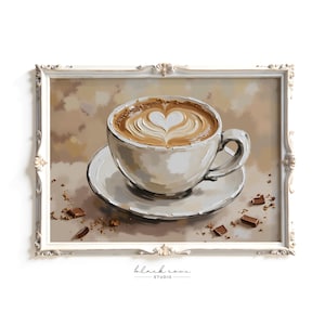May include: A framed print depicting a coffee cup with heart-shaped latte art. The cup rests on a saucer, with scattered chocolate pieces. The white frame has decorative detailing. The background is a soft, neutral colour.