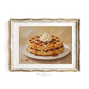 May include: A framed print of two golden-brown waffles stacked on a white plate, drizzled with syrup and topped with whipped cream. The artwork is set against a neutral background and framed in a gold ornate frame. The print is from Black Cove Studio.