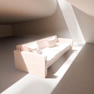 May include: A light-coloured wooden sofa with two matching pillows. The sofa has a minimalist design with a slatted back and sides. The cushions and pillows are a soft, neutral colour. The sofa is in a bright, sunlit room.