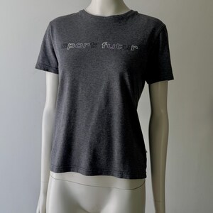 Peut inclure: T-shirt gris fonc&eacute; avec l'inscription "sport futur" en blanc soulign&eacute; sur la poitrine. Le t-shirt a des manches courtes et un col rond. Le v&ecirc;tement est pr&eacute;sent&eacute; sur un mannequin.