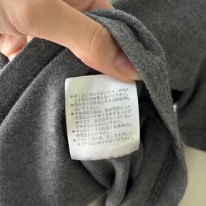 Peut inclure: Gros plan sur un t-shirt gris fonc&eacute; avec une &eacute;tiquette blanche. L'&eacute;tiquette contient du texte japonais avec des instructions d'entretien. Le t-shirt est fait d'un tissu doux et textur&eacute;.