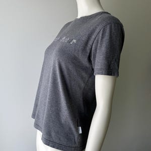 Peut inclure: Un t-shirt gris fonc&eacute; avec le mot "future" en blanc, dans une police stylis&eacute;e sur la poitrine. Le t-shirt &agrave; manches courtes est fait d'une mati&egrave;re douce et comporte une petite &eacute;tiquette blanche sur le c&ocirc;t&eacute;.