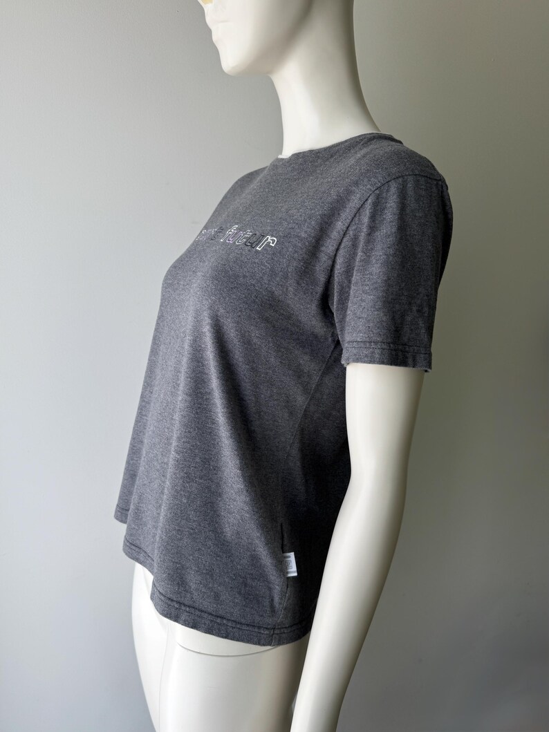 Peut inclure: Un t-shirt gris fonc&eacute; avec le mot "future" en blanc, dans une police stylis&eacute;e sur la poitrine. Le t-shirt &agrave; manches courtes est fait d'une mati&egrave;re douce et comporte une petite &eacute;tiquette blanche sur le c&ocirc;t&eacute;.