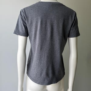 Peut inclure: Un t-shirt gris avec un col en V et des manches courtes, pr&eacute;sent&eacute; sur un mannequin. Le tissu semble &ecirc;tre une mati&egrave;re douce et chin&eacute;e. Le t-shirt a un ourlet incurv&eacute;.