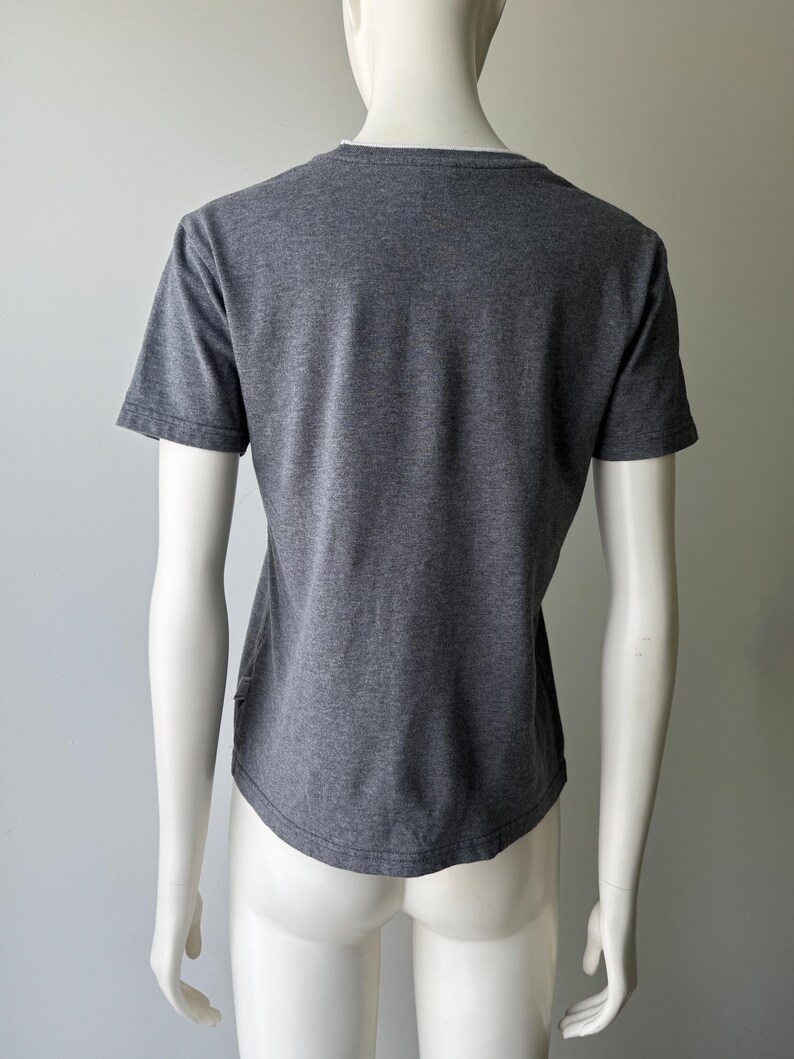 Peut inclure: Un t-shirt gris avec un col en V et des manches courtes, pr&eacute;sent&eacute; sur un mannequin. Le tissu semble &ecirc;tre une mati&egrave;re douce et chin&eacute;e. Le t-shirt a un ourlet incurv&eacute;.