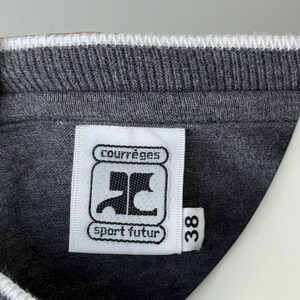 Peut inclure: Gros plan sur un col de sweat-shirt gris avec une bordure blanche. Une &eacute;tiquette blanche affiche le logo "Courr&egrave;ges" et le texte "sport futur". Le num&eacute;ro "38" est imprim&eacute; sur l'&eacute;tiquette.