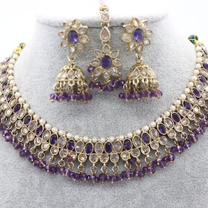 May include: A purple and white gemstone necklace and earrings set. The necklace features a layered design with multiple strands of purple beads and white pearls. The earrings are dangle style with a purple gemstone center and a bell-shaped pendant.