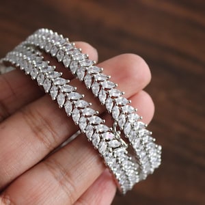 Peut inclure: Deux bracelets argentés avec une rangée de pierres claires en forme de marquise serties dans un motif de feuilles.