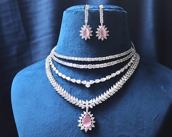 May include: A multi-layered silver necklace with a pink teardrop pendant and matching earrings. The necklace features a delicate chain with a larger, more ornate pendant.