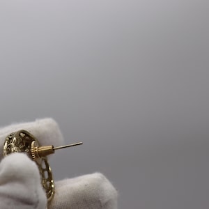 Op de afbeelding: Gouden oorbellen met een gedetailleerd, ingewikkeld ontwerp. De oorbellen hebben een post-sluiting.