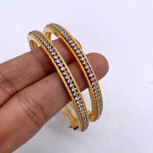May include: Two gold bangles with a row of clear stones around the edge.
