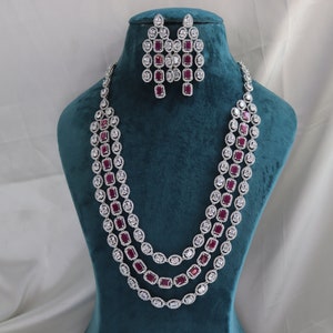 Puede incluir: Un collar de plata de tres hilos con una fila de piedras cuadradas rosas y una fila de piedras redondas blancas en cada hilo. El collar se muestra en un busto de maniquí de terciopelo turquesa. También se incluyen pendientes a juego con piedras cuadradas rosas y piedras redondas blancas.