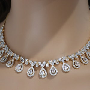 May include: A gold-toned necklace featuring a series of clear, teardrop-shaped pendants, each surrounded by smaller, sparkling stones. The necklace has a delicate, elegant design, perfect for special occasions.