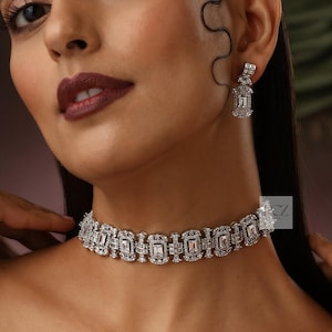 May include: A dazzling silver-toned necklace and matching earrings set. The necklace is a choker style, featuring rectangular and square-cut stones. The earrings have a similar design, with a rectangular stone suspended from a square stud. The jewelry sparkles.