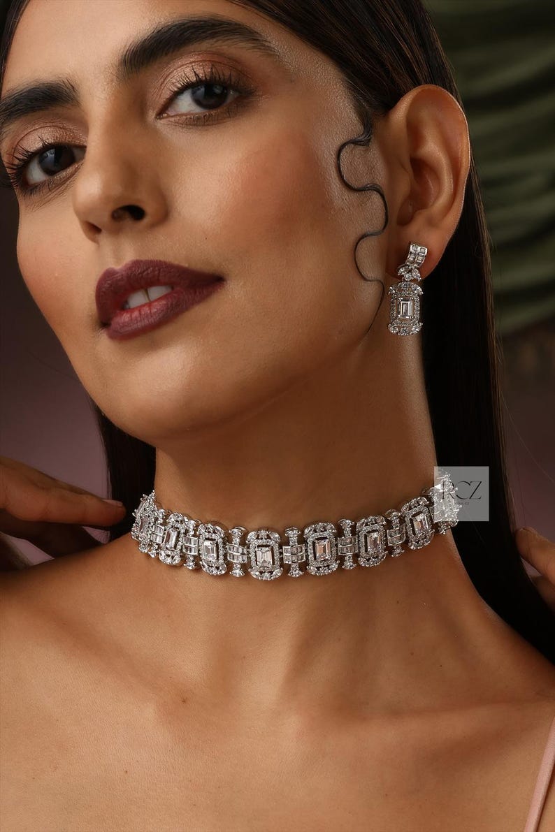 May include: A dazzling silver-toned necklace and matching earrings set. The necklace is a choker style, featuring rectangular and square-cut stones. The earrings have a similar design, with a rectangular stone suspended from a square stud. The jewelry sparkles.