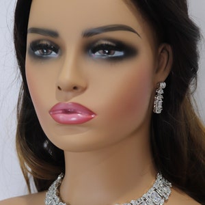 May include: A dazzling silver-toned necklace and matching earrings set. The necklace features a series of rectangular and square-cut stones, complemented by smaller accent stones. The earrings have a similar design, creating a cohesive and elegant jewelry ensemble.