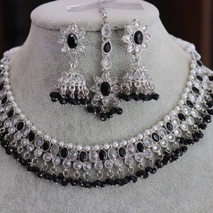 Puede incluir: Un collar y pendientes de plata con piedras blancas y negras. El collar tiene un diseño en capas con cuentas negras y perlas blancas. Los pendientes son de estilo colgante con un centro de piedra negra.