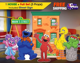 May include: A set of five Sesame Street character cutouts including Abby Cadabby, Cookie Monster with cookies, Elmo, Big Bird, and Oscar the Grouch in a trash can, alongside a cardboard house facade and a green street sign reading MARK'S STREET.