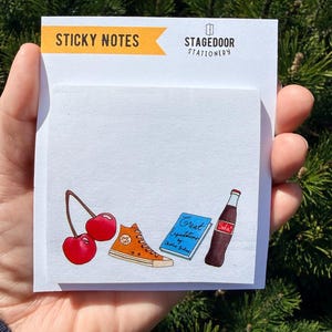 May include: White sticky notes pad with illustrations of cherries, an orange sneaker, a book titled "Great Expectations", and a soda bottle. The top of the pad has the text "STICKY NOTES" and "STAGEDOOR STATIONERY".