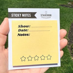 May include: A yellow sticky note pad with the words "Sticky Notes" at the top and "Stagedoor Stationery" on the right. The pad has lines for "Show:" "Date:" and "Notes:" with five star icons at the bottom.