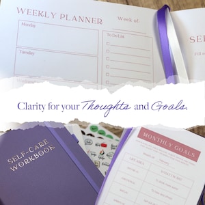 May include: A purple self-care workbook and weekly planner are open, displaying sections for goals and to-do lists. The text "Clarity for your Thoughts and Goals" is visible. Stickers and a ribbon bookmark are also present.