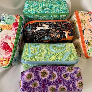 May include: A collection of five rectangular fabric zipper pouches featuring diverse patterns including green floral, black with a rabbit and deer, paisley in green and blue, large pink roses, and purple daisies, each with a coordinating zipper.