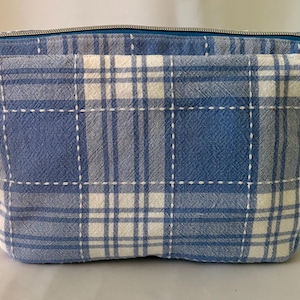 May include: A blue and white plaid zippered pouch with a white stitched design.