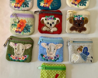 Può includere: Una collezione di piccole borsette ricamate in vari colori. I disegni includono fiori tropicali, koala, agnelli, una fatina dei denti e un uccello rosso. Ogni borsetta ha una chiusura a cerniera e una combinazione di colori unica.