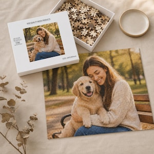 Peut inclure: Un puzzle en bois carré représentant une photographie d'une personne serrant un chiot golden retriever sur un banc de parc. La boîte blanche affiche la même image, le texte HIGH QUALITY WOOD PRODUCTS, JIGSAW PUZZLES, 196 et SIZE: 280x280mm.