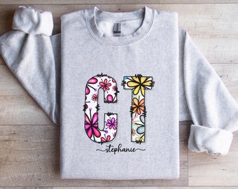 May include: A gray sweatshirt with the letters "CT" in large, colorful, floral print. The letters are outlined in black and the name "Stephanie" is written in cursive below the letters.