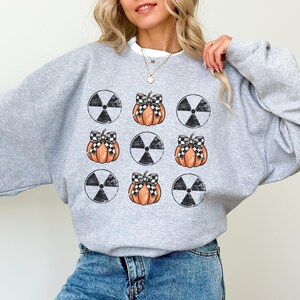May include: A gray sweatshirt with a pattern of black and white radiation symbols and orange pumpkins with black and white checkered bows.