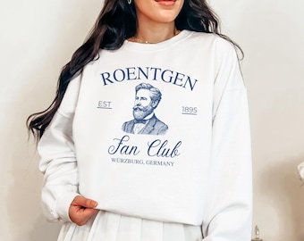 May include: White sweatshirt with a blue graphic that reads "ROENTGEN Fan Club" with a portrait of a man and the text "WURZBURG, GERMANY". The sweatshirt also has the text "EST 1895".