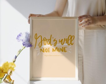 May include: A framed print with a peach background and white frame. The print features the text "God's will not mine" in gold lettering with a white line under "will". The text "#goodnessandgrace" is in smaller lettering below the main text.
