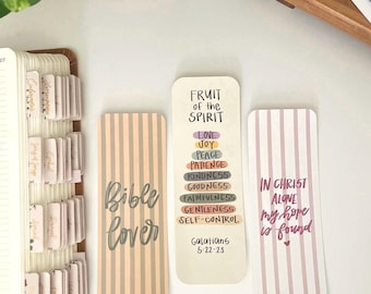 May include: Three decorative bookmarks with inspirational quotes. One bookmark has vertical peach and gray stripes and the words "Bible Cover". Another bookmark has a list of virtues and the text "Fruit of the Spirit". The third bookmark has pink and white stripes and the text "In Christ Alone my hope is found".