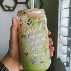 May include: A green glass tumbler with a bamboo lid and a clear plastic straw. The tumbler has a floral design and the text "Consider how the wildflowers grow" and "Luke 12:27".