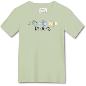 May include: A light green short-sleeved t-shirt featuring three embroidered fish in shades of green, blue, and yellow. The name "BROOKS" is embroidered below the fish. The shirt is made of a soft material.