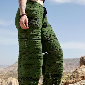 May include: Green crochet trousers with black detailing and a drawstring. The trousers have a distinctive textured pattern with openwork sections. These handmade trousers are made from a soft material, ideal for a bohemian or casual look.