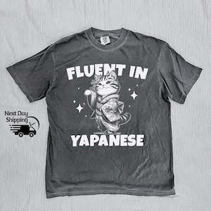 May include: A black t-shirt with a white graphic of a cat in a kimono. The text "Fluent in Japanese" is printed below the cat.