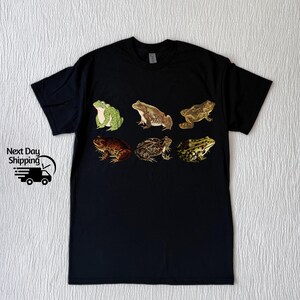 May include: Black t-shirt with a graphic print of six different frogs in various poses. The frogs are green, brown, and tan.