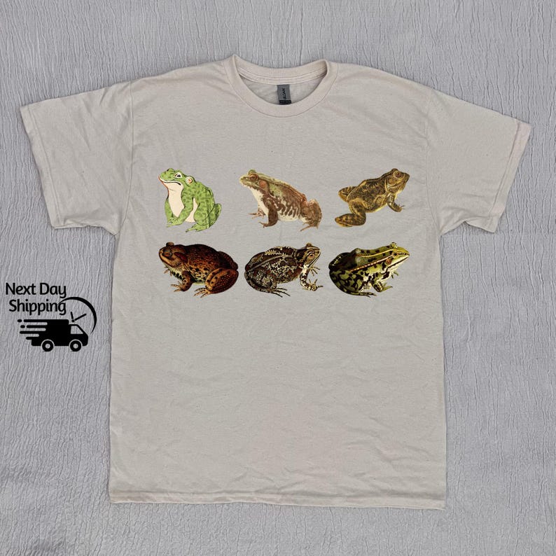May include: A light gray t-shirt with a graphic print of six different frogs in various poses. The frogs are in shades of green, brown, and black.