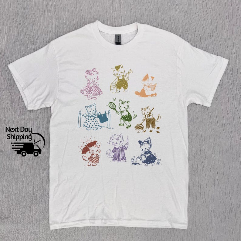 K&ouml;nnte beinhalten: Wei&szlig;es T-Shirt mit einem bunten Grafikdruck von Katzen, die Sport treiben und Hausarbeiten erledigen. Die Katzen tragen verschiedene farbige Kleidung und haben unterschiedliche Gesichtsausdr&uuml;cke.