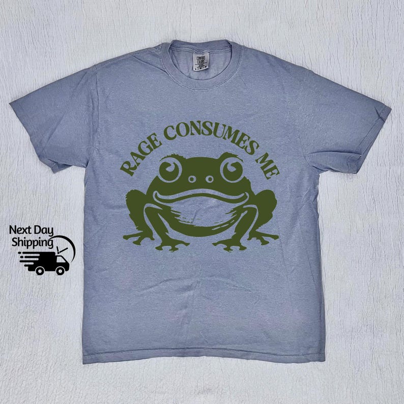 May include: A light blue t-shirt with a green frog graphic and the text "Rage Consumes Me".