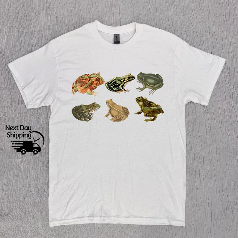 Puede incluir: Camiseta blanca con un gr&aacute;fico de seis ranas diferentes en varias poses. Las ranas son verdes, marrones y naranjas con marcas negras.